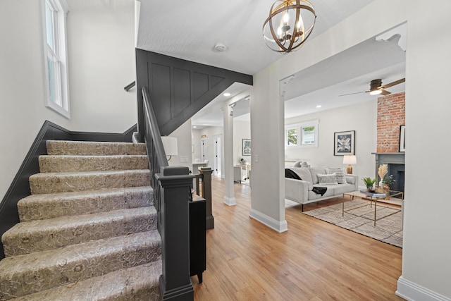 stairs with a fireplace, wood-type flooring, and ceiling fan with notable chandelier