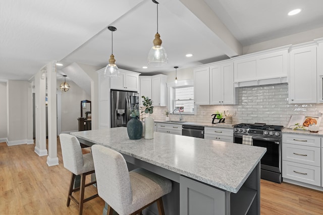 kitchen with light wood-type flooring, stainless steel appliances, sink, white cabinets, and a kitchen island