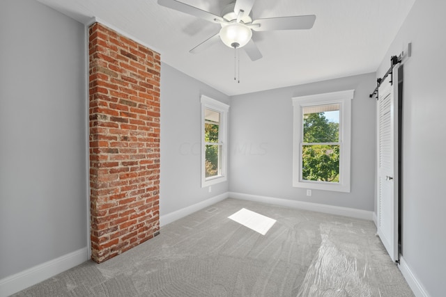 unfurnished bedroom featuring a barn door, ceiling fan, and light carpet