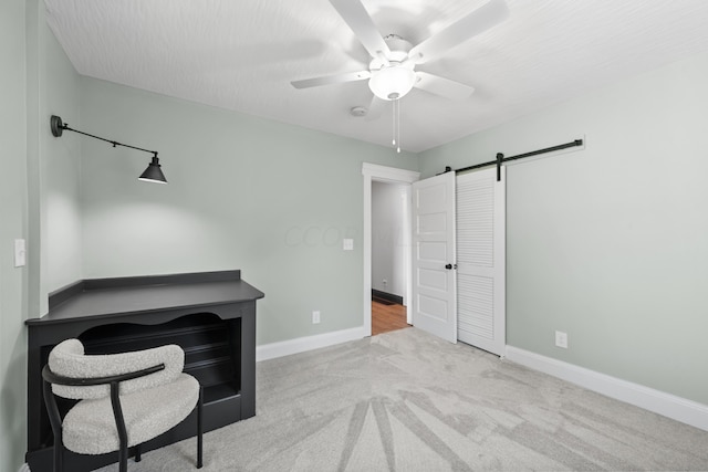 unfurnished office featuring ceiling fan, a barn door, and light carpet