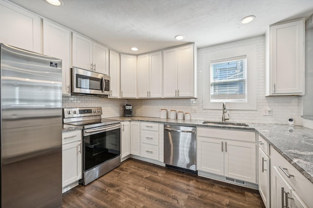 kitchen with appliances with stainless steel finishes, light stone counters, dark wood-type flooring, sink, and white cabinets