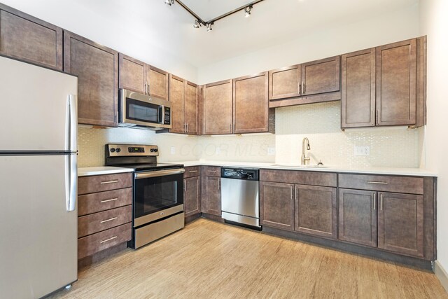 kitchen featuring track lighting, sink, decorative backsplash, light wood-type flooring, and appliances with stainless steel finishes