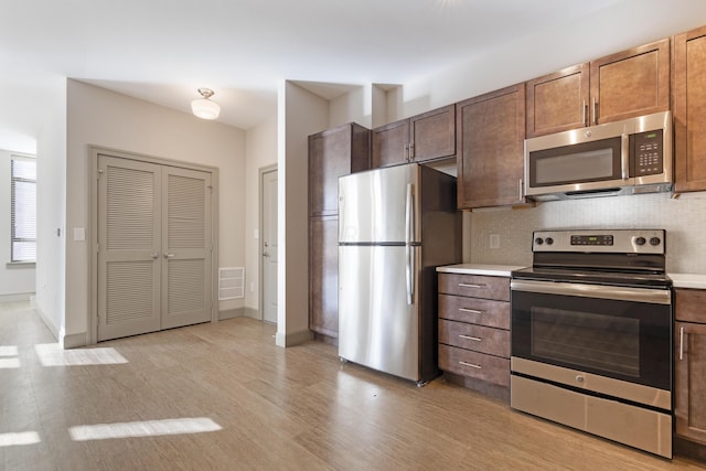 kitchen with light wood-type flooring, backsplash, and appliances with stainless steel finishes