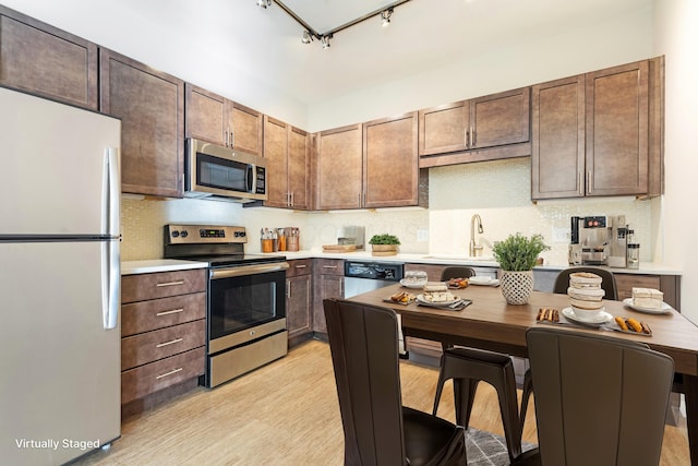 kitchen with rail lighting, sink, appliances with stainless steel finishes, dark brown cabinets, and light hardwood / wood-style floors