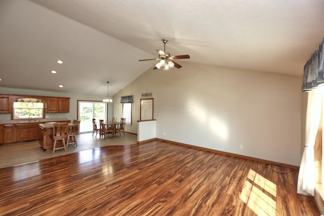 unfurnished living room with high vaulted ceiling, dark hardwood / wood-style floors, sink, and ceiling fan with notable chandelier