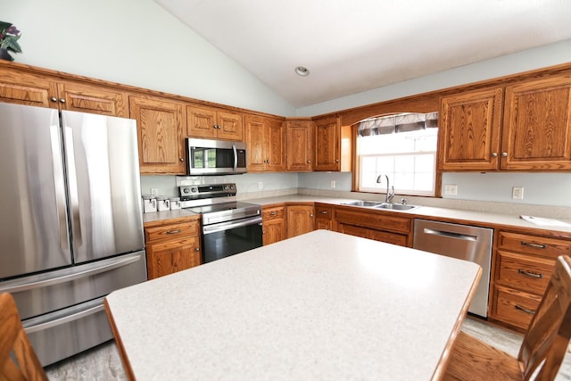 kitchen featuring brown cabinetry, vaulted ceiling, stainless steel appliances, and a sink