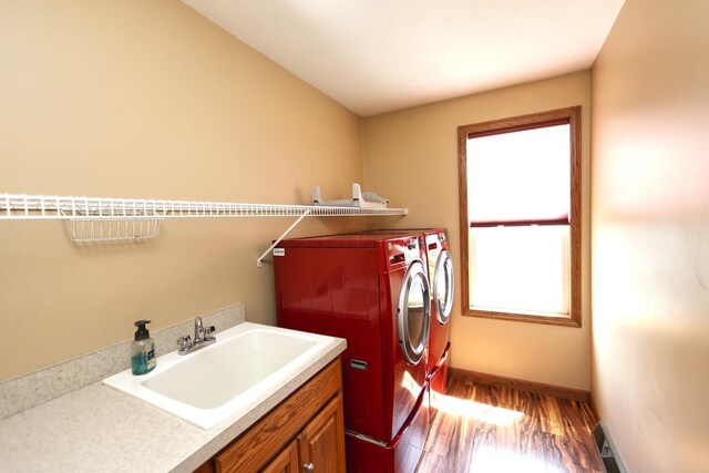 clothes washing area featuring washing machine and clothes dryer, a sink, baseboards, wood finished floors, and cabinet space