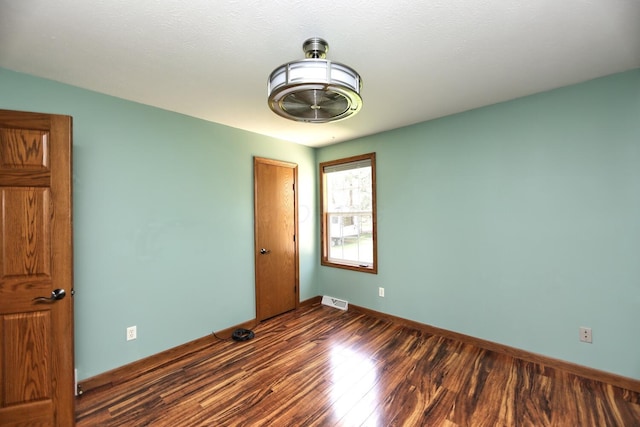 empty room featuring baseboards, dark wood-style flooring, and visible vents