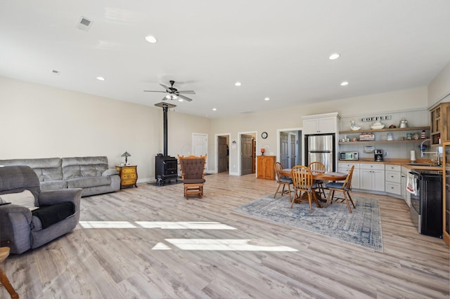 living room with light wood-type flooring, a wood stove, and ceiling fan