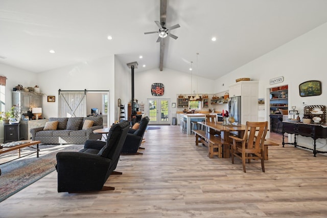 living room featuring high vaulted ceiling, ceiling fan, a barn door, beam ceiling, and light hardwood / wood-style floors