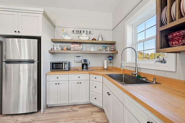 kitchen featuring light wood-type flooring, stainless steel appliances, sink, white cabinets, and butcher block counters