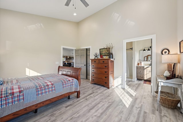 bedroom with ensuite bathroom, ceiling fan, light wood-type flooring, and a towering ceiling