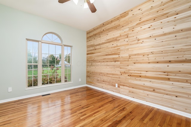 spare room featuring light hardwood / wood-style floors, ceiling fan, and wooden walls