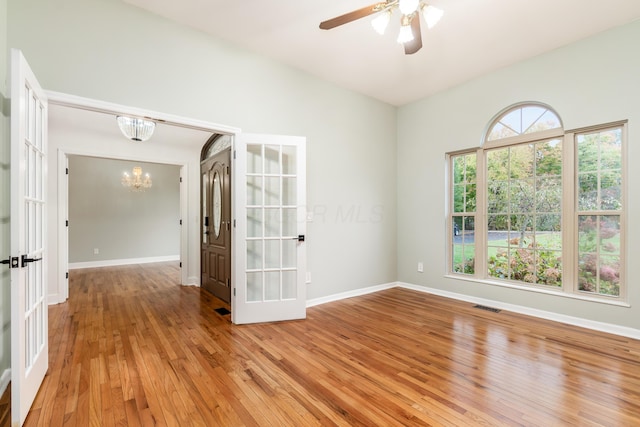 unfurnished room with ceiling fan with notable chandelier, french doors, and light wood-type flooring