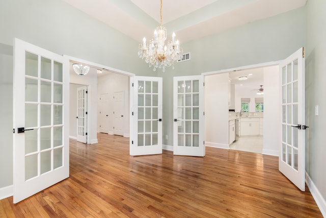 unfurnished dining area with french doors, ceiling fan with notable chandelier, and light wood-type flooring