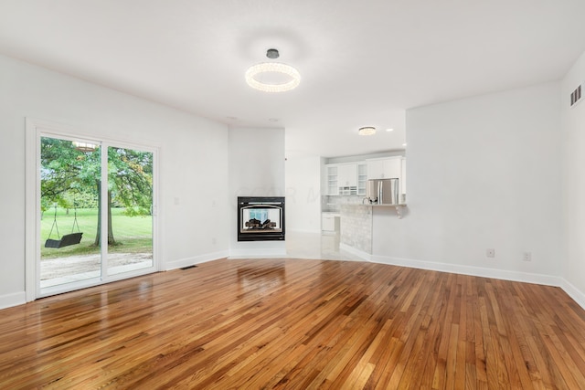 unfurnished living room featuring a multi sided fireplace and light hardwood / wood-style flooring