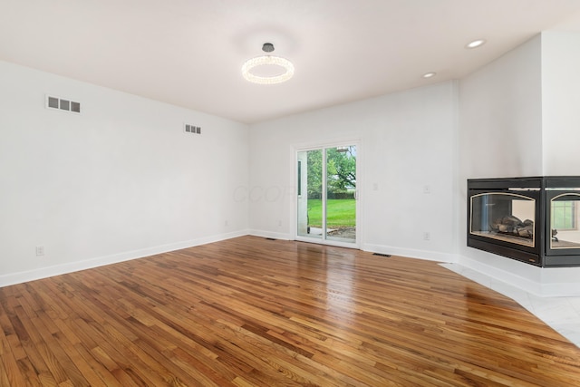 unfurnished living room featuring a multi sided fireplace and hardwood / wood-style floors