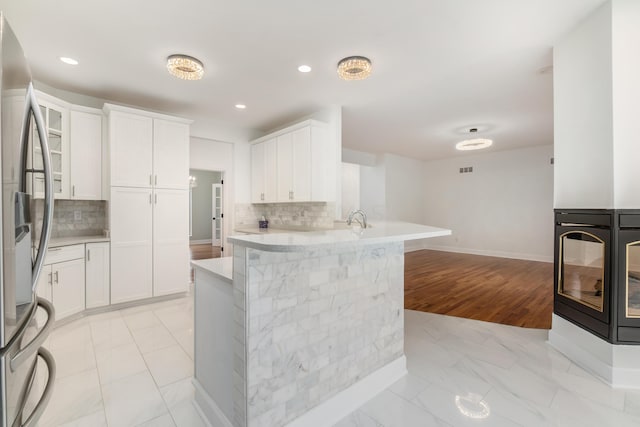 kitchen featuring backsplash, stainless steel fridge, white cabinetry, and kitchen peninsula