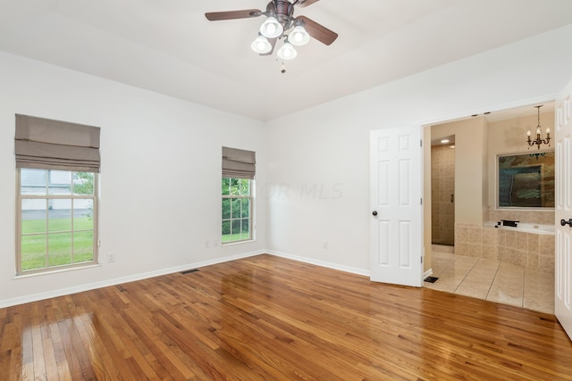 unfurnished room featuring ceiling fan with notable chandelier, light wood-type flooring, and plenty of natural light