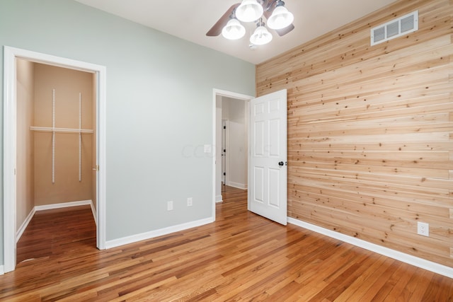 unfurnished bedroom with light hardwood / wood-style floors, wooden walls, and a closet