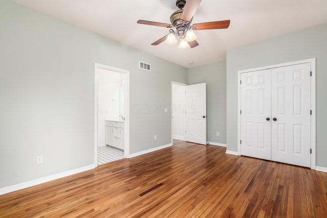 unfurnished bedroom featuring ensuite bath, ceiling fan, a closet, and wood-type flooring