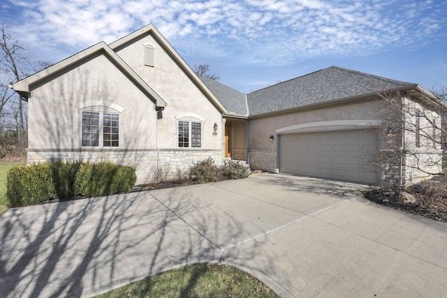 french country inspired facade with a garage, stone siding, driveway, roof with shingles, and stucco siding