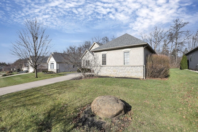 view of side of property featuring a shingled roof, stone siding, a yard, driveway, and stucco siding