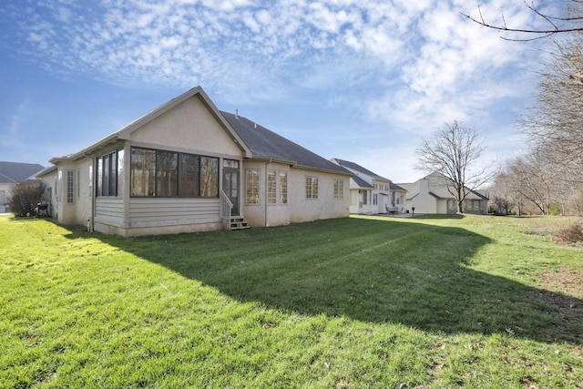 back of property featuring entry steps, a lawn, a sunroom, and stucco siding