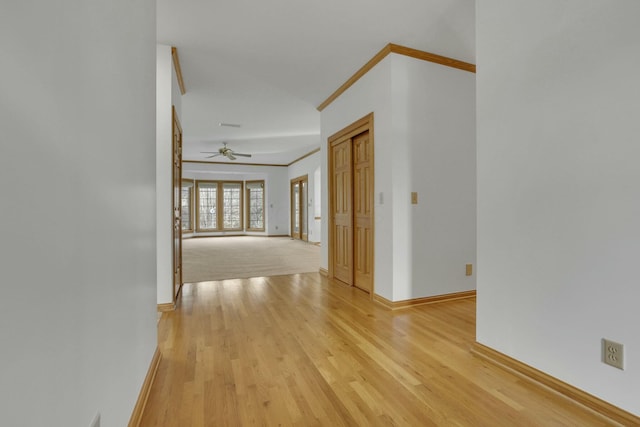 corridor with light wood-style flooring, baseboards, and crown molding