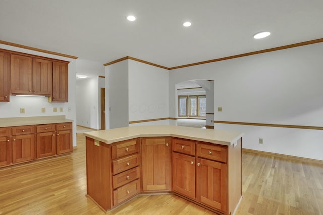 kitchen with light countertops, brown cabinetry, light wood-type flooring, and crown molding