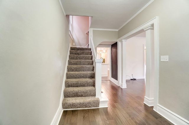 staircase with ornate columns, wood-type flooring, and ornamental molding