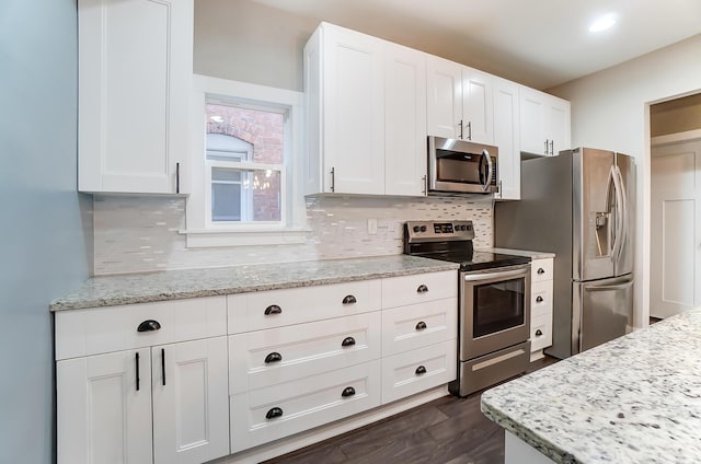 kitchen with dark wood-type flooring, white cabinets, decorative backsplash, light stone counters, and stainless steel appliances