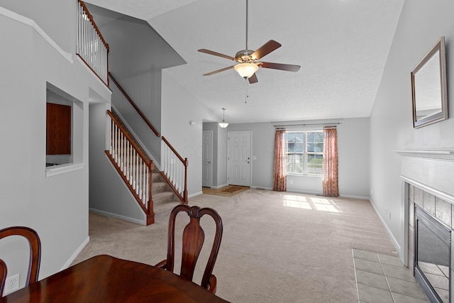 unfurnished dining area featuring a tile fireplace, light carpet, high vaulted ceiling, and ceiling fan