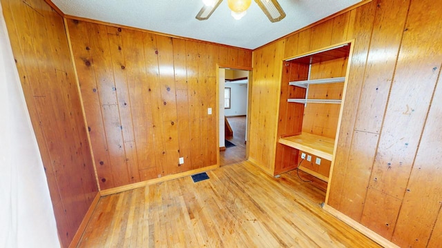 unfurnished bedroom featuring light hardwood / wood-style floors, ceiling fan, and wood walls