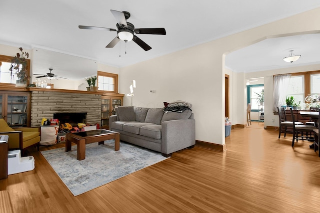 living room with a stone fireplace, a wealth of natural light, light hardwood / wood-style flooring, and ceiling fan