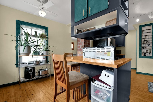 kitchen with blue cabinetry, ceiling fan, wood counters, hardwood / wood-style floors, and track lighting