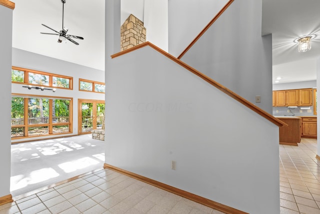 unfurnished living room with ceiling fan, french doors, a towering ceiling, and light tile patterned flooring