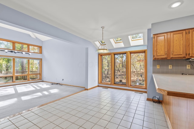 kitchen with vaulted ceiling with skylight, decorative light fixtures, light tile patterned floors, and tasteful backsplash