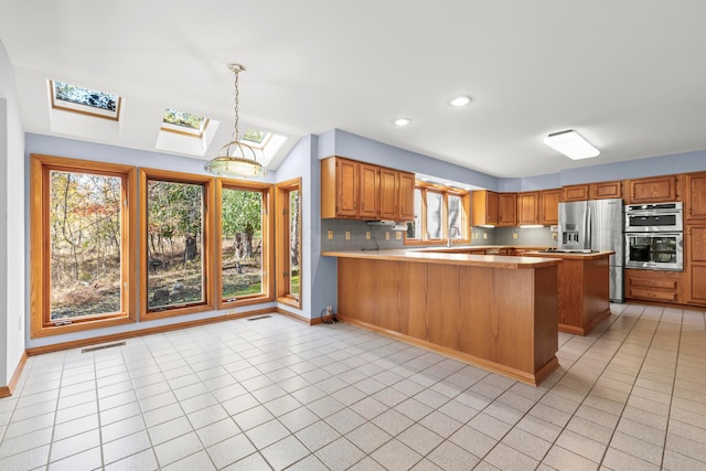 kitchen featuring kitchen peninsula, a skylight, stainless steel appliances, decorative light fixtures, and light tile patterned flooring