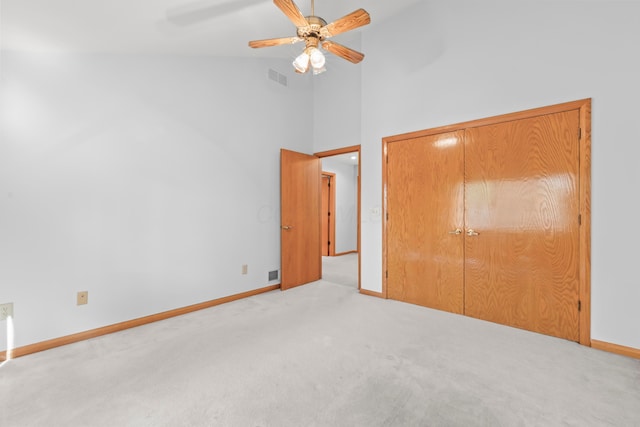 unfurnished bedroom featuring light carpet, a closet, high vaulted ceiling, and ceiling fan