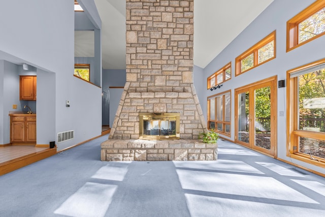 living room featuring a high ceiling, light colored carpet, and a stone fireplace