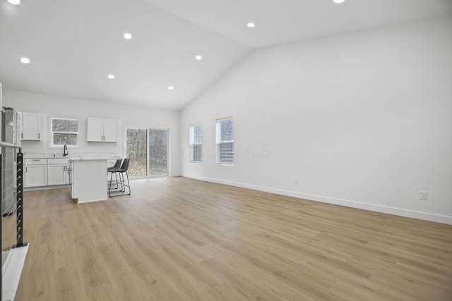 unfurnished living room with a healthy amount of sunlight, light wood-type flooring, and high vaulted ceiling