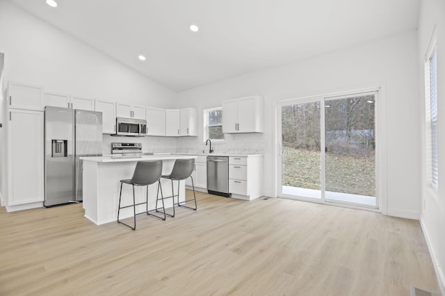 kitchen featuring a breakfast bar, a center island, white cabinets, light hardwood / wood-style floors, and stainless steel appliances