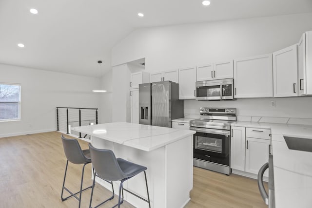 kitchen featuring pendant lighting, vaulted ceiling, light hardwood / wood-style floors, white cabinetry, and stainless steel appliances