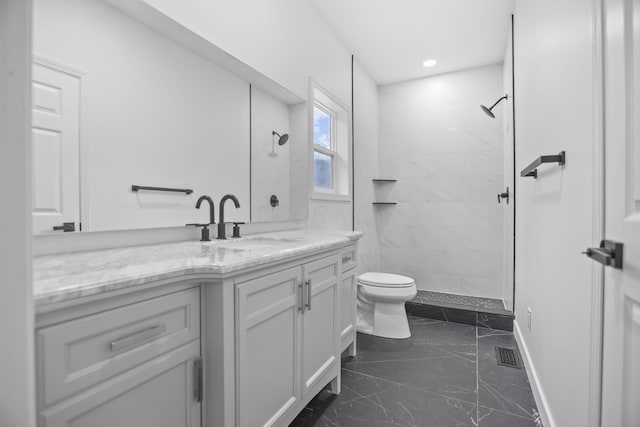 bathroom with a tile shower, vanity, and toilet