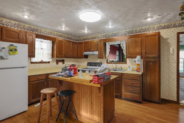 kitchen featuring sink, light hardwood / wood-style flooring, a textured ceiling, white appliances, and a breakfast bar