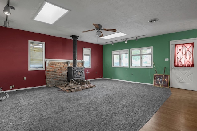 unfurnished living room with track lighting, a textured ceiling, ceiling fan, hardwood / wood-style flooring, and a wood stove