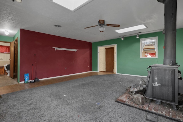 unfurnished living room featuring a textured ceiling, ceiling fan, a wood stove, and dark wood-type flooring