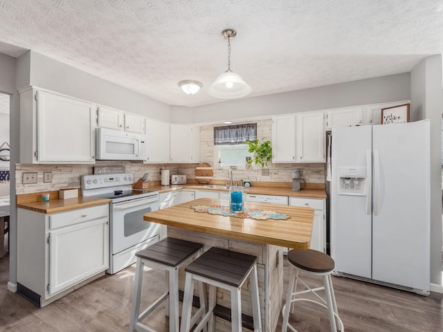 kitchen featuring white cabinetry, sink, light hardwood / wood-style flooring, pendant lighting, and white appliances