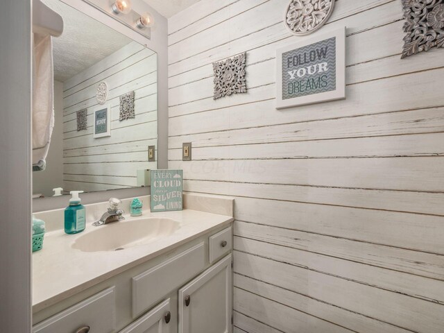 bathroom featuring wood walls, vanity, and a textured ceiling